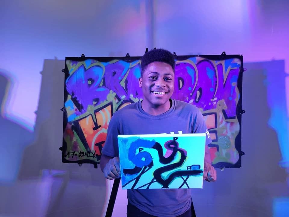 Young man holding his artwork with a purplish-blue artsy background